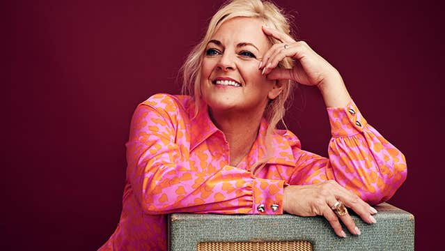 A smiling woman in pink shirt leaning on a table