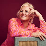 A smiling woman in pink shirt leaning on a table