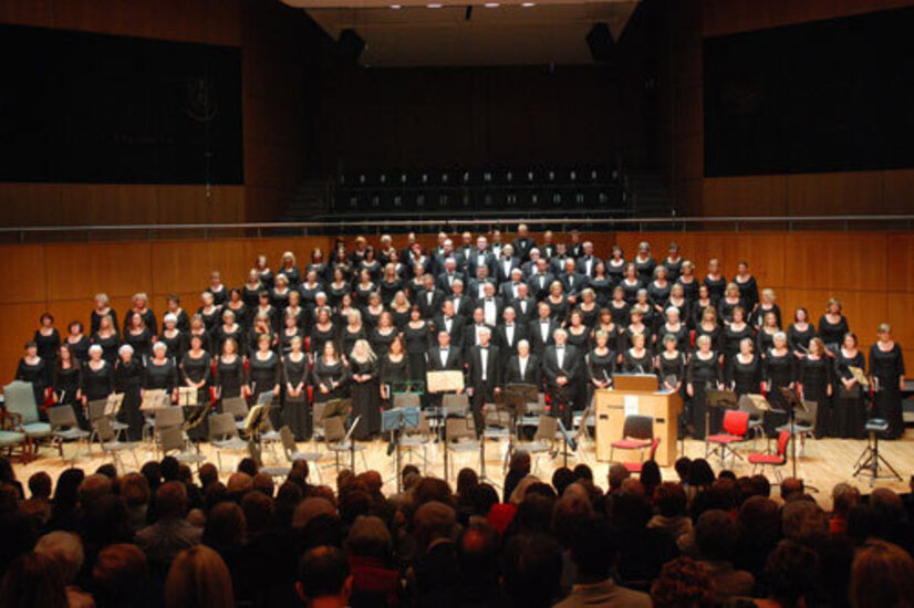 A distant shot of a large choir standing in tiers on a large stage, seen from the audience.