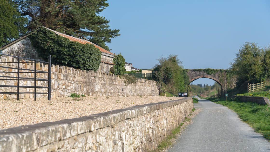 A walking path beside a stone wall continuing towards a stone bridge