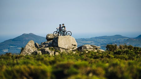 Two people with bicycles standing on a large rock overlooking the landscape