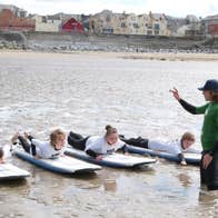 Four kids on surfboards on the stand with an instructor giving lessons