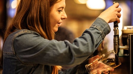 A woman behind a bar about the pull a pint