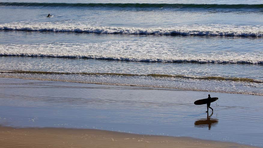 A surfer walks along the beach in Inch Stand, Dingle, Kerry