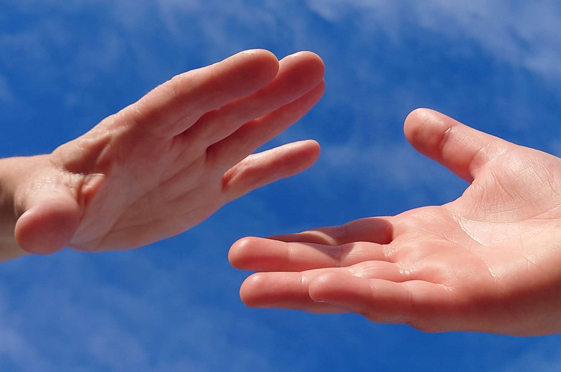 Close up shot of 2 hands reaching out about to touch against a bright blue sky