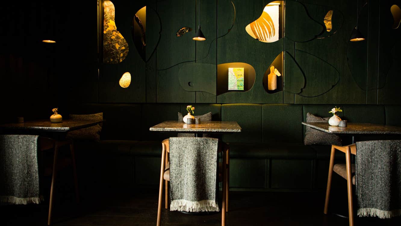 Three tables and chairs with grey scarfs on the back in a restaurant with dark green walls