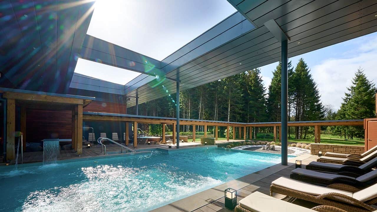 Outdoor pool surrounded by wooden decking and loungers with cushions