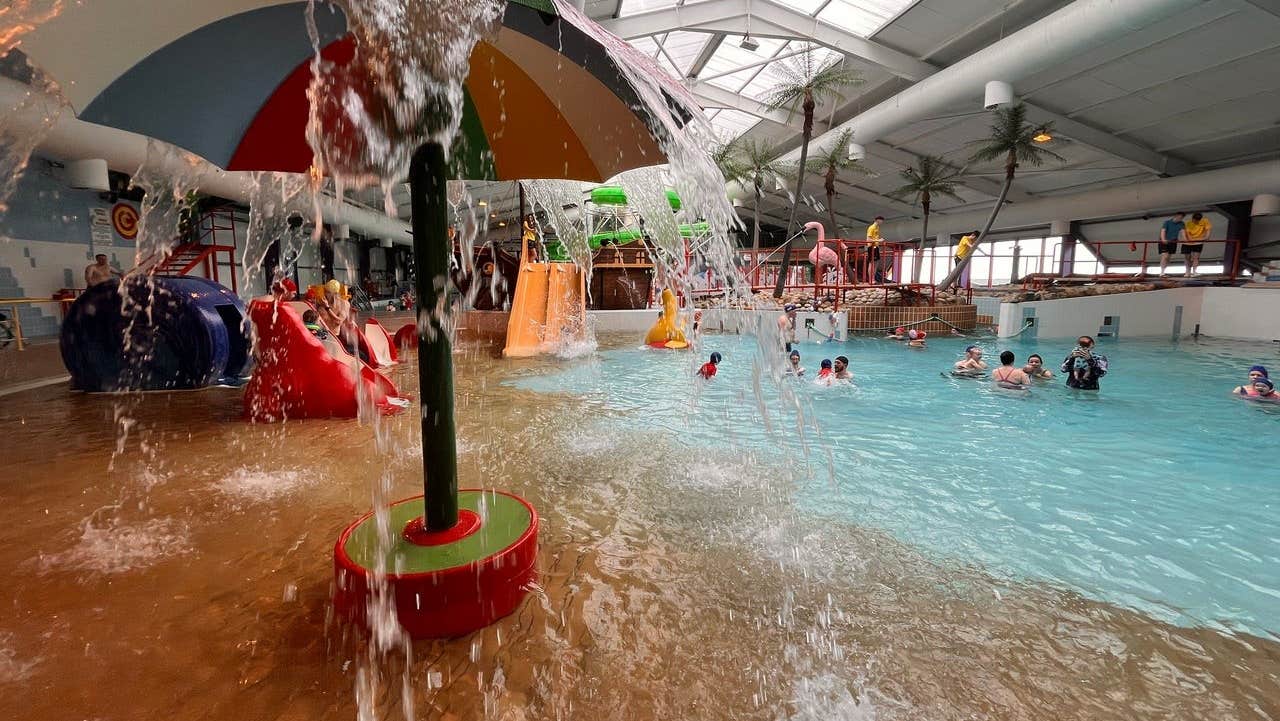 A multicoloured umbrella with water spilling from it into a swimming pool