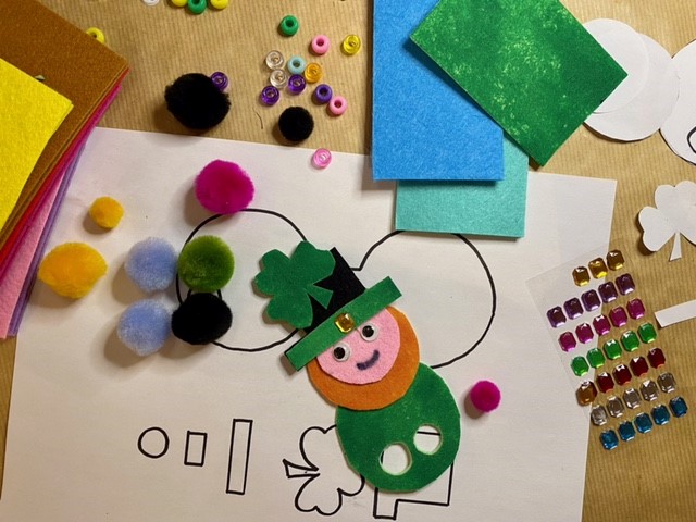 Different coloured craft items, paper and sticky jewels, and image of leprechaun in different coloured felts.