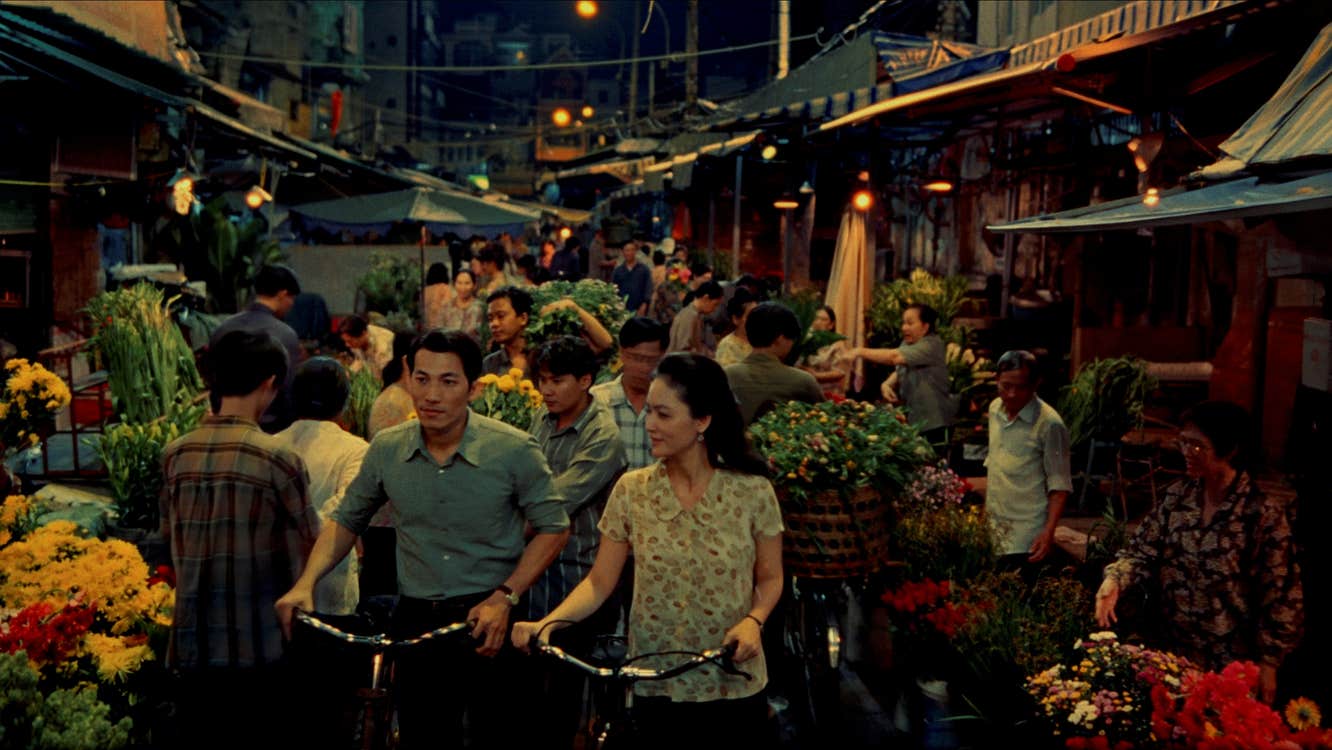A man and a woman with bicycles are walking through a market.