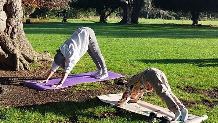 A child and adult outdoors each on a mat in a yoga pose.