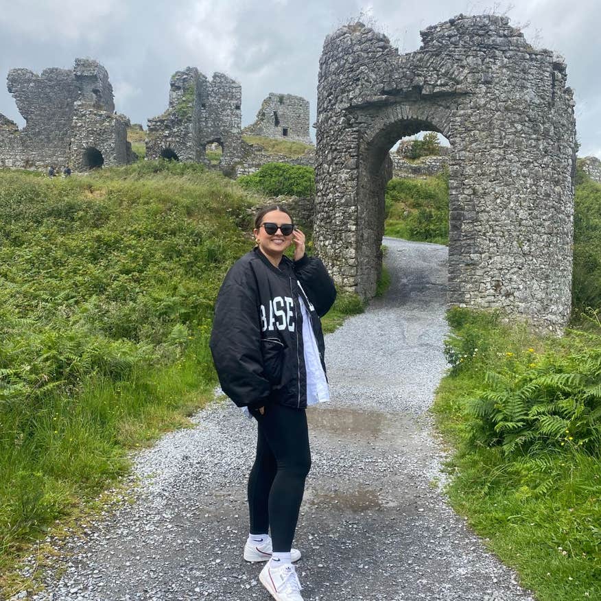 A woman wearing black standing in front of the ruins at the Rock of Dunamase in Laois.