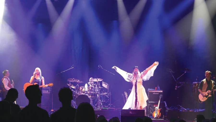 4 people on a stage playing musical instruments and singing.