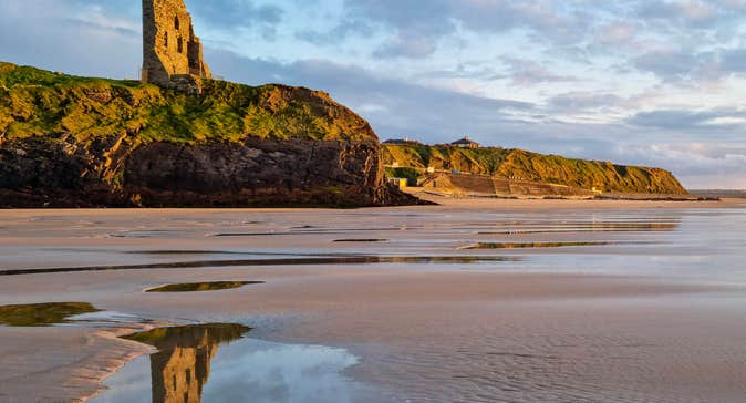 Ballybunion castle on cliff reflected in water on the beach below