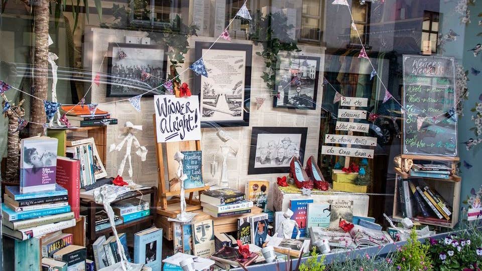A shop window with lots of different books with paper figures, bunting and pictures in frames.