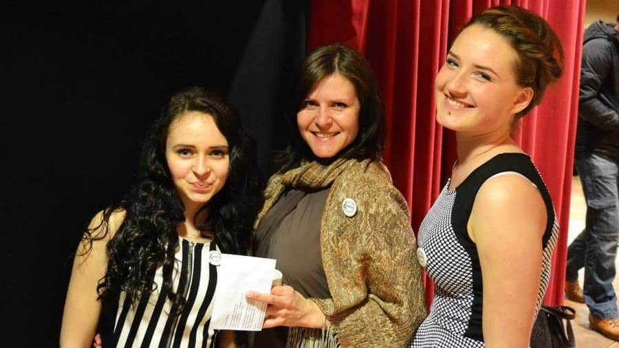 Three people standing by stage curtains smiling at the camera
