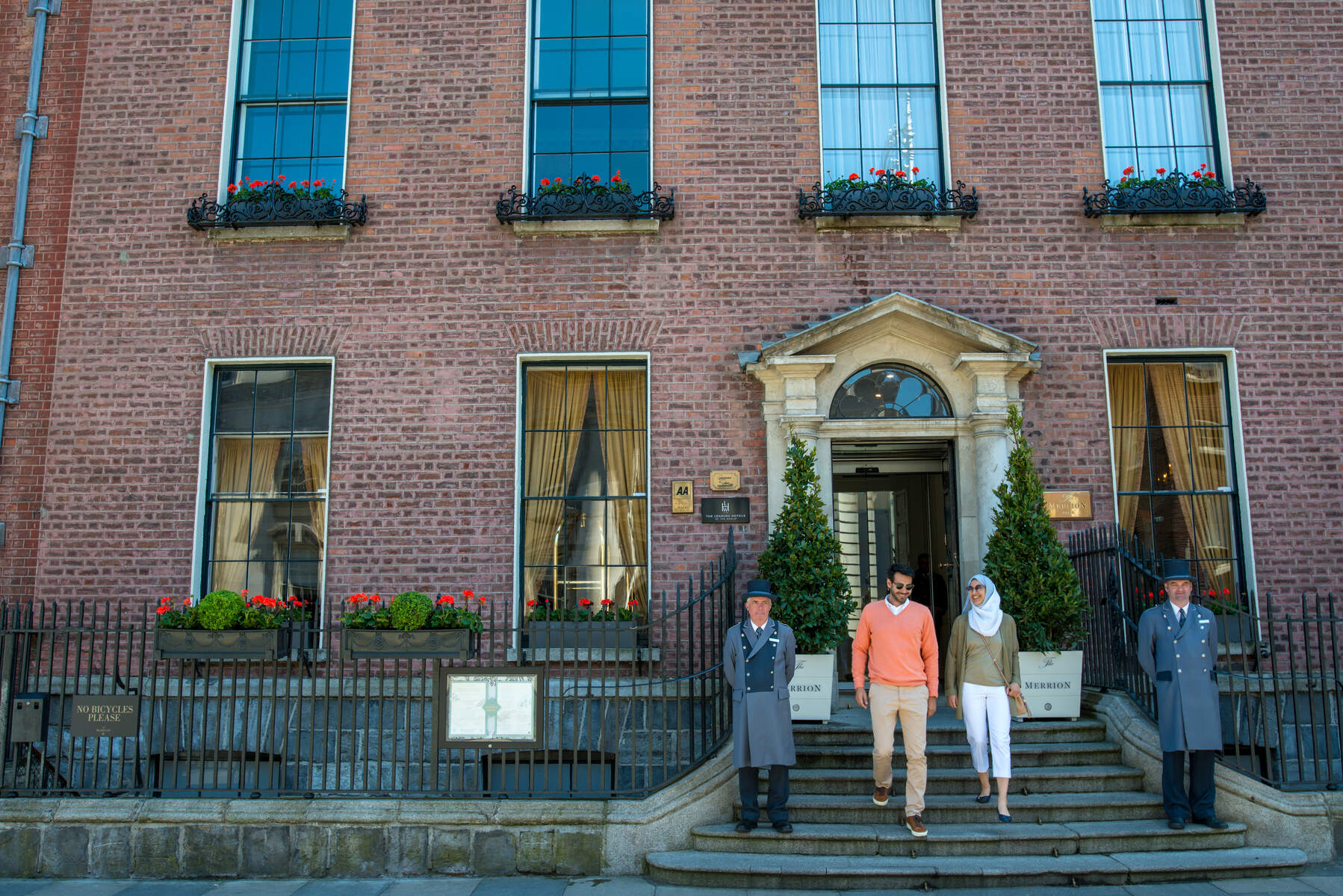 Exterior of The Merrion Hotel in Dublin, with a couple walking down stairs flanked by two uniformed doormen.