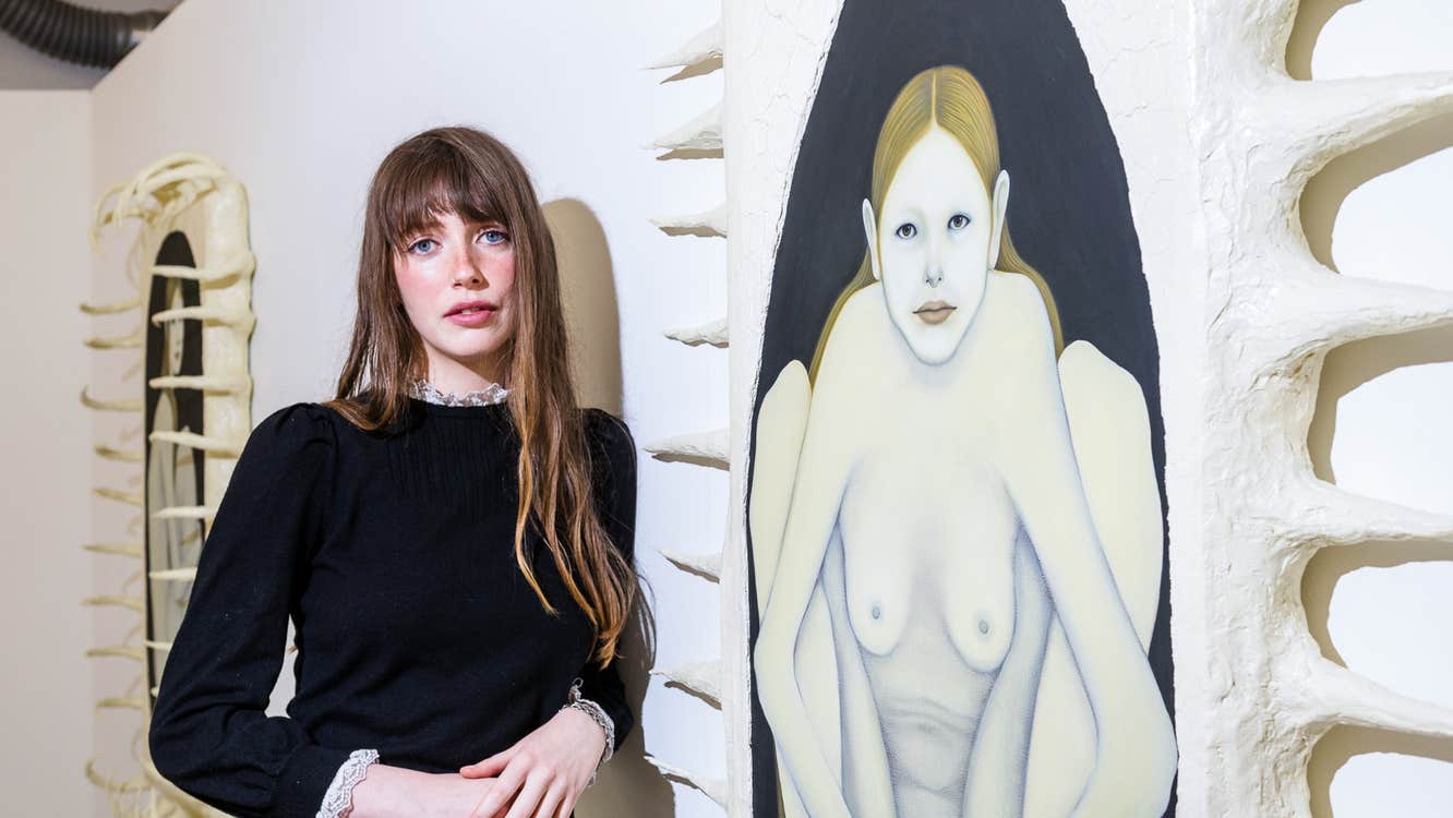A woman next to a painting of a naked woman.