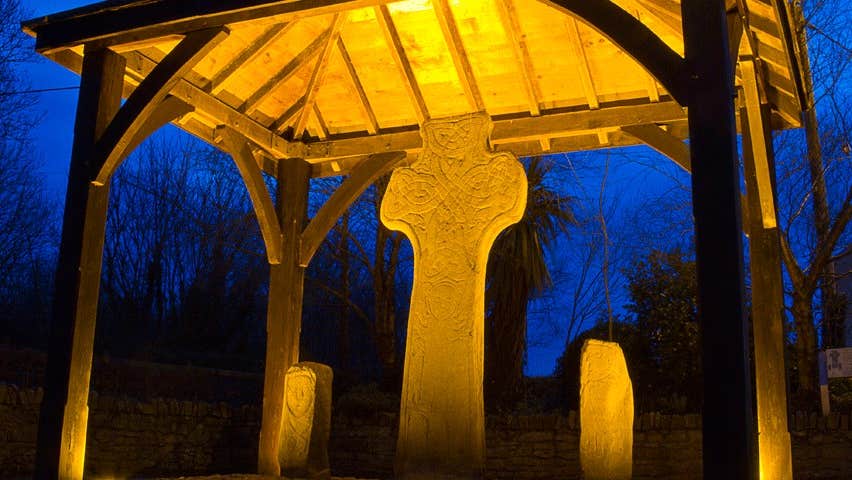 An ancient stone cross lit up at night