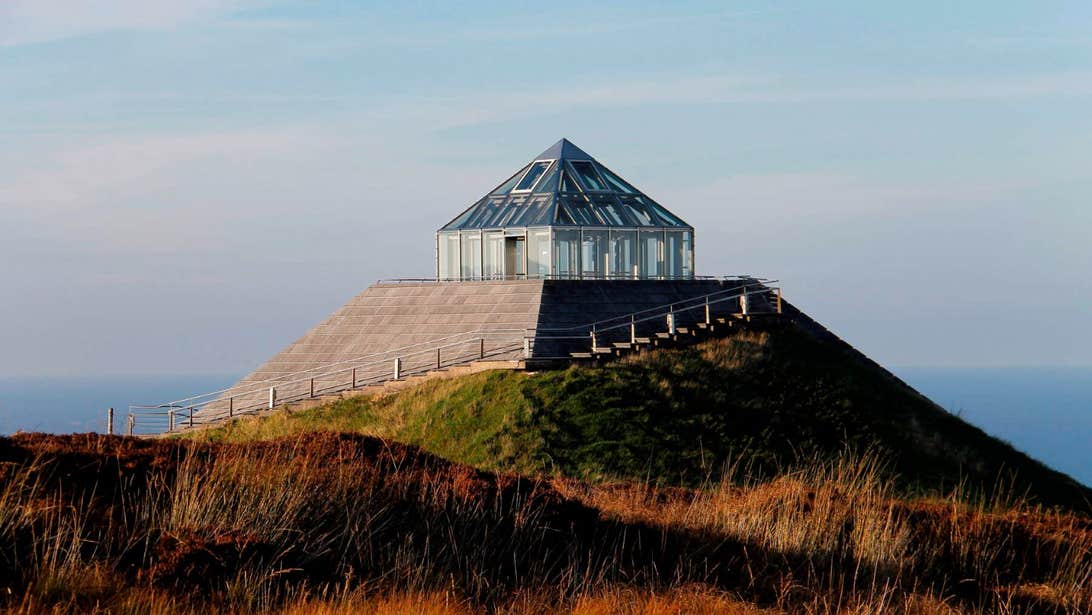 Ceide Fields Visitor Centre rises above on a hill with the Atlantic Ocean in the background.
