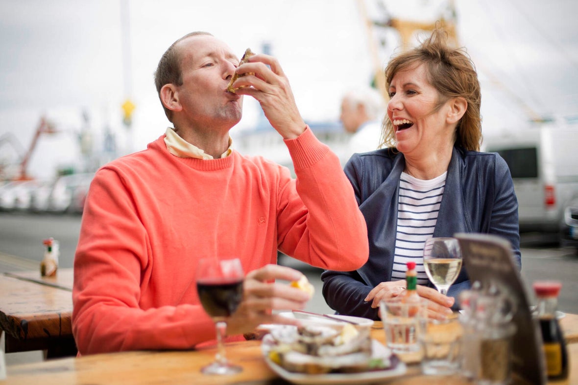 A couple sitting outside a seafood restaurants sucking back oysters with glasses of wine.