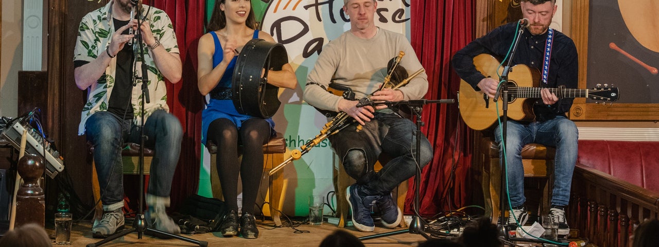 Four musicians playing instruments on a stage at the Irish House Party