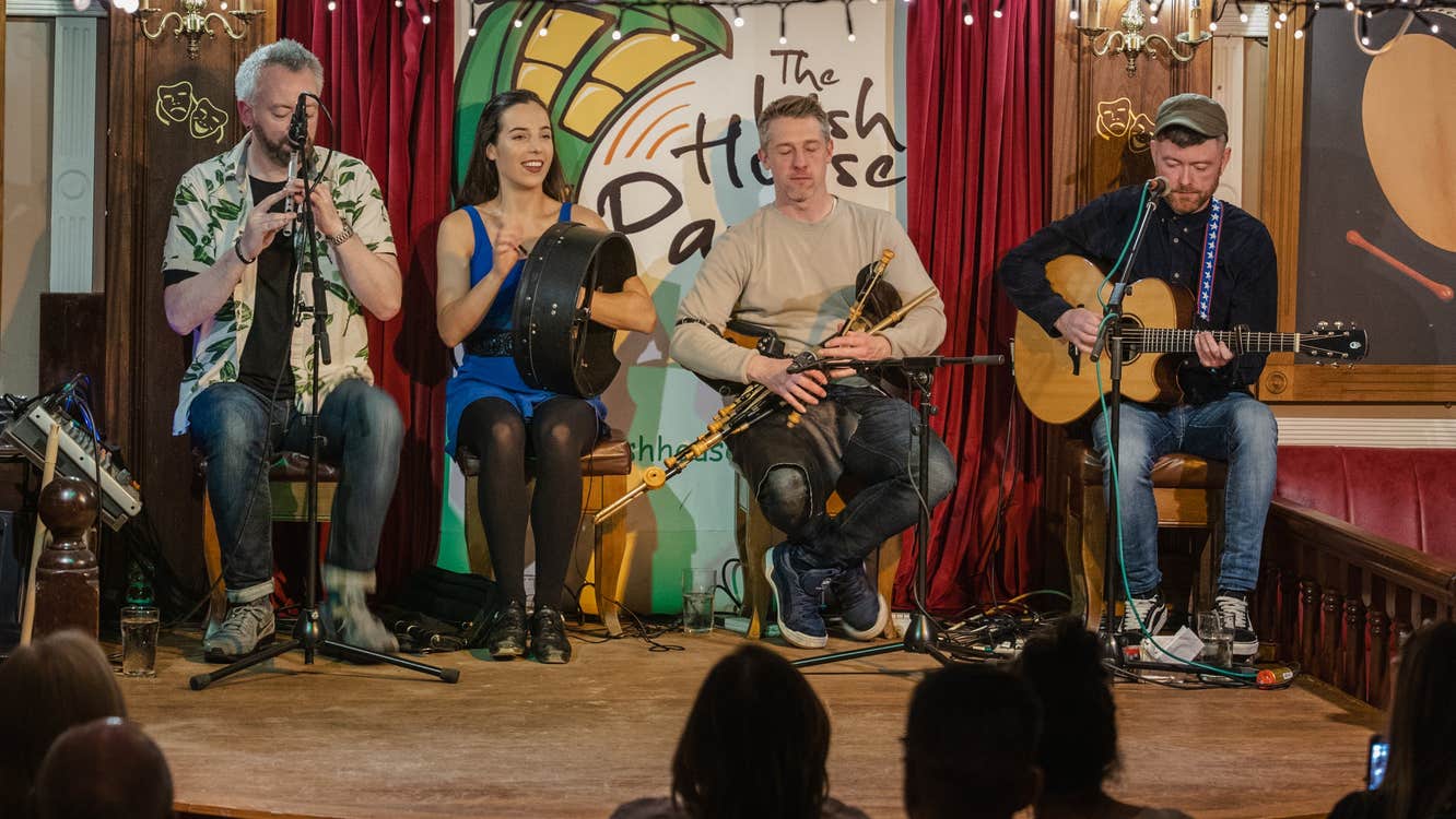 Four musicians playing instruments on a stage at the Irish House Party