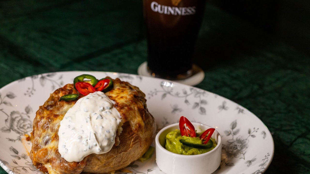 A main course served on a plate alongside a small bowl of green dip with a pint of Guinness in the background