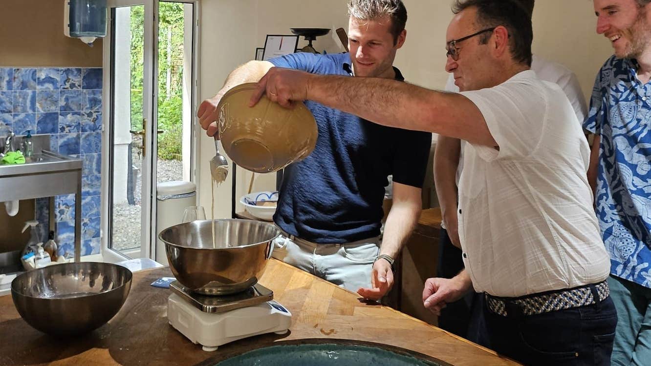 People standing at a kitchen counter watching as a cook pours ingredients into a mixing bowl