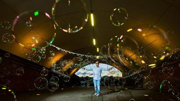 Distant view of man with arms outstretched in pale blue with area covered in bubbles of different sizes.