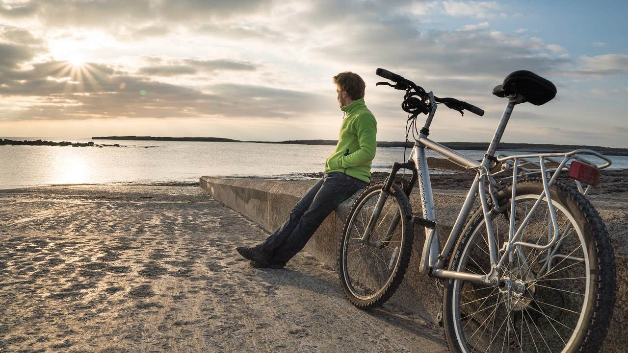 A man looking out to sea sitting on a beach next to his ebike from Ebike Aran Islands