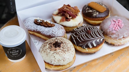 A box of colourful doughnuts on a counter beside a coffee cup