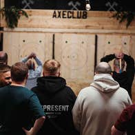 Two people throwing axes as a group of people watch