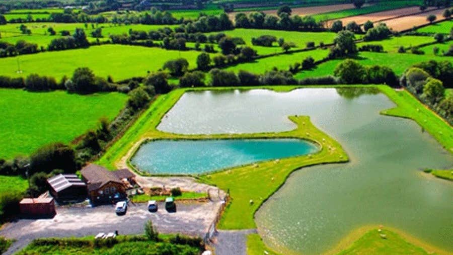 An aerial view of Ardaire Angling Centre with the building to the left and the lake pools to the right with green fields and trees in the background
