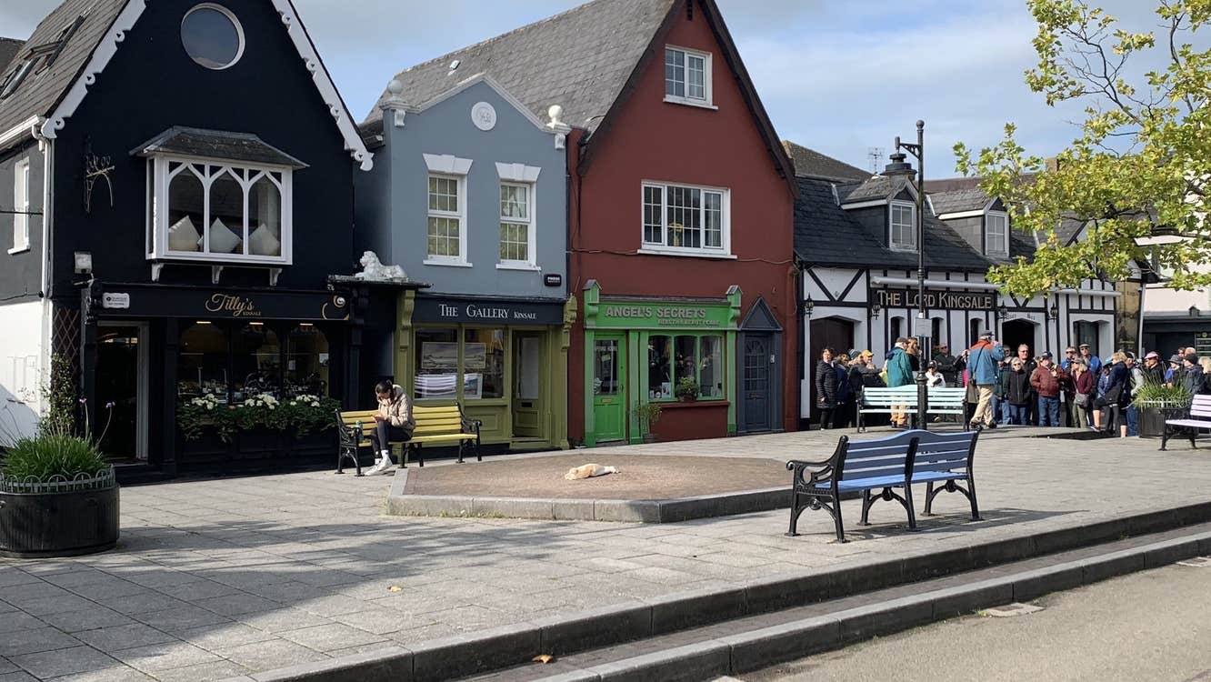 Four buildings to the left of a raised paved area with seating and a group of people to the right