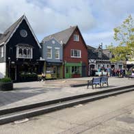 Four buildings to the left of a raised paved area with seating and a group of people to the right