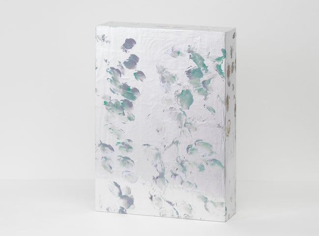 A photo of a small free-standing painting with green and purple daubled brush marks on a silver surface