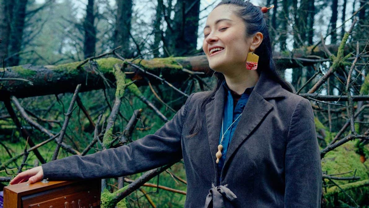 A smiling woman with eyes closed, outdoors with bare trees behind.