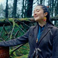 A smiling woman with eyes closed, outdoors with bare trees behind.