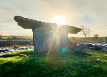 View of a sunrise behind a portal dolmen with Anam Croí Ireland Tours