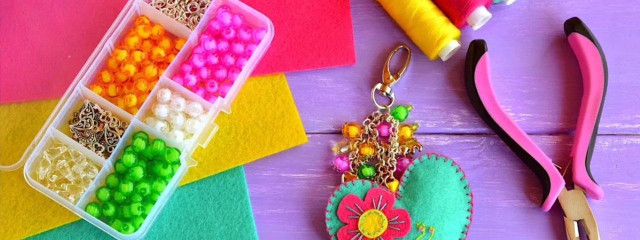 Looking down on a work surface with threads, pliers, a box with different coloured beads and a heart shaped keyring.