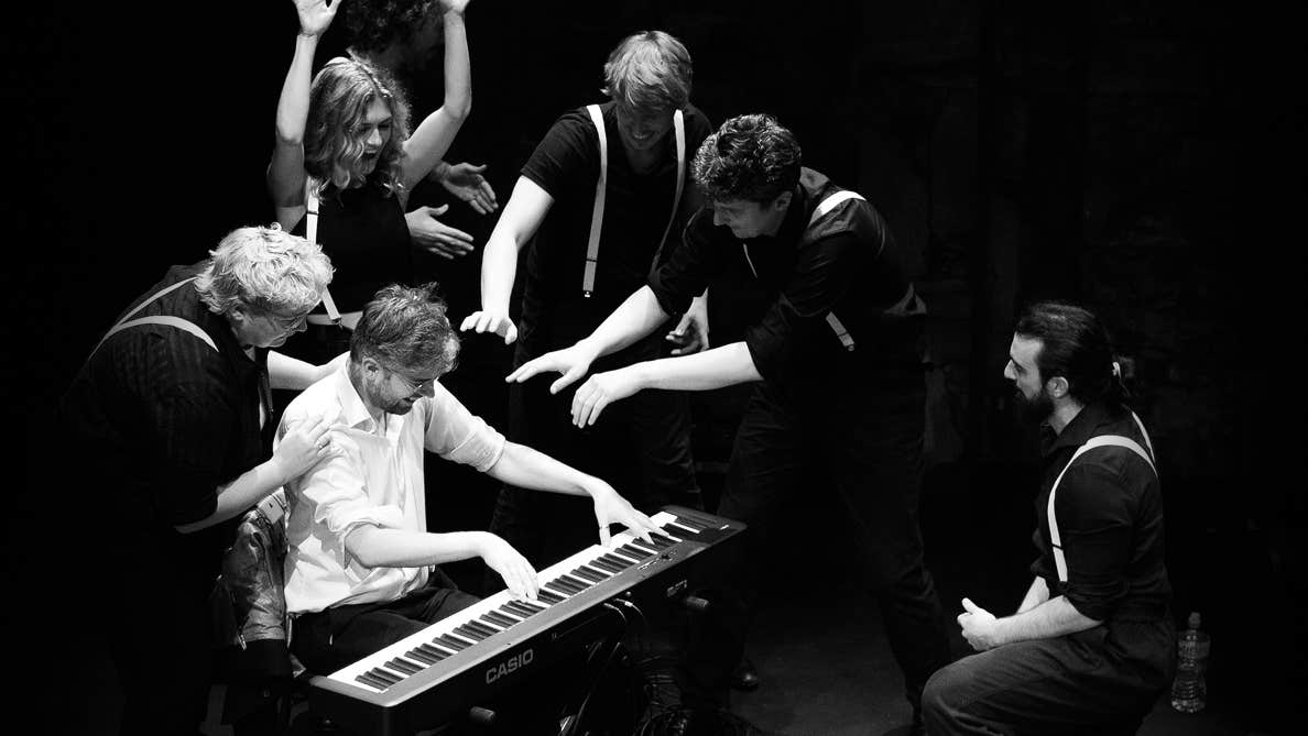 Black and white photo of group of people gathered around person on a keyboard.