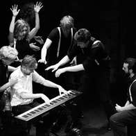Black and white photo of group of people gathered around person on a keyboard.