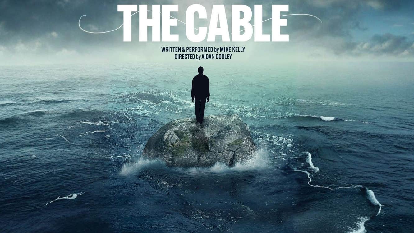 In a stormy, dark sea a single figure is standing on a rock out of the water.