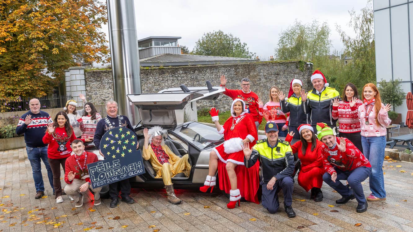 Féile Lonrach – Festival of Glow, Carlow - a group of smiling and waving people in Christmas jumpers around a silver sports car.