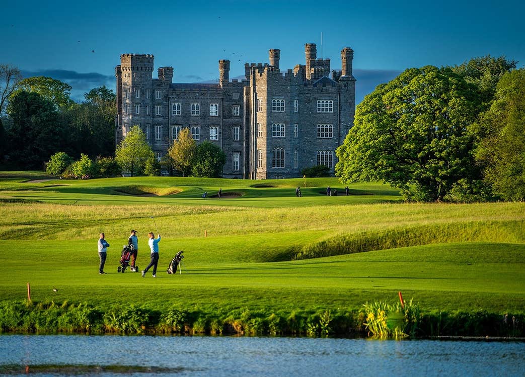 Golfers on a golf course beside a lake with a castle in the distance