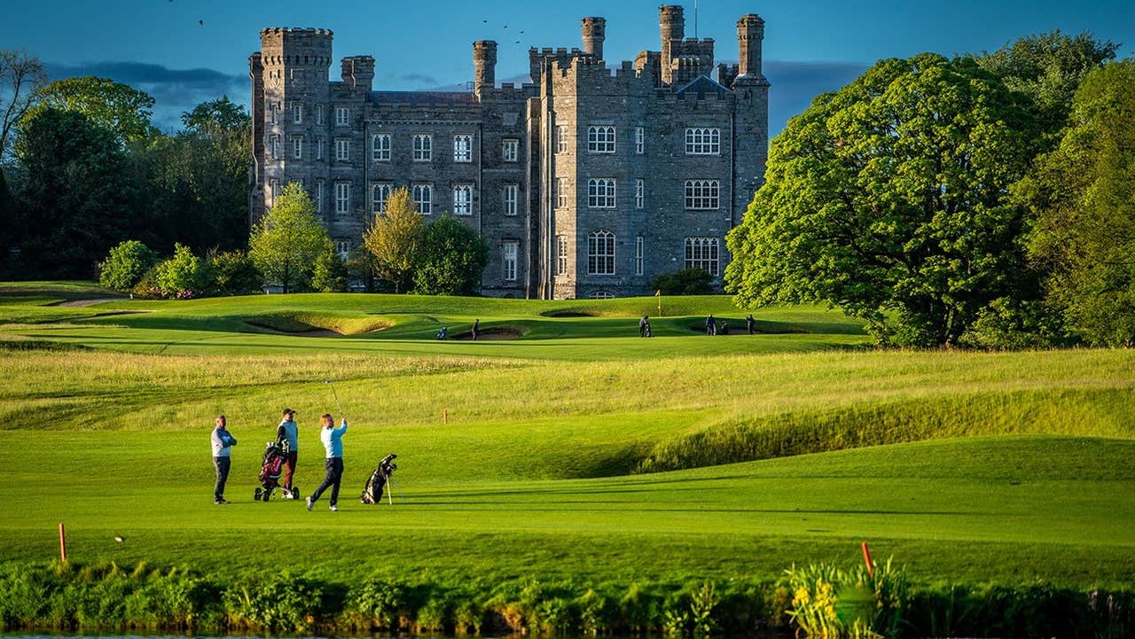 Golfers on a golf course beside a lake with a castle in the distance