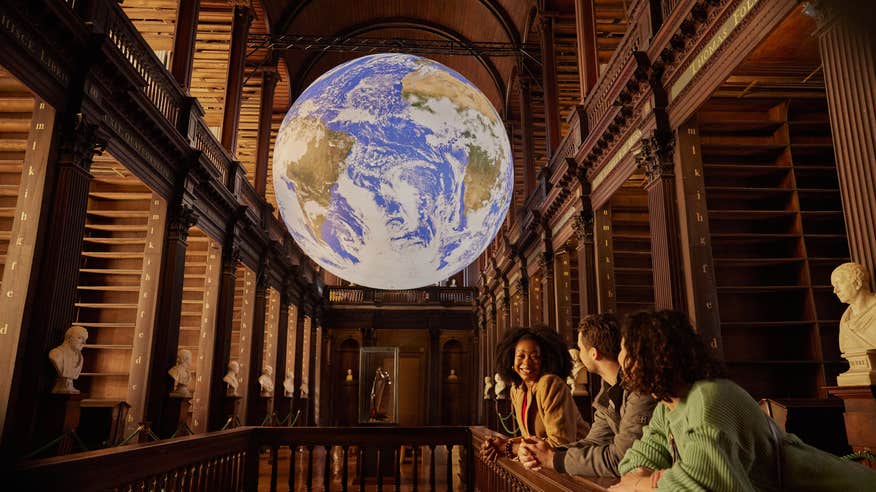 Gaia sculpture hanging above three people at Trinity's Old Library.