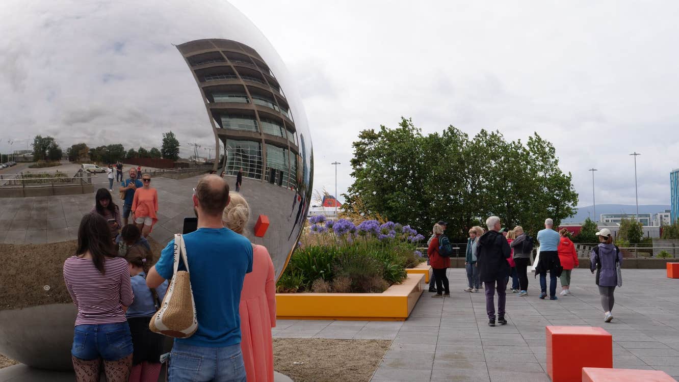 People looking at a large metal sphere in a city street