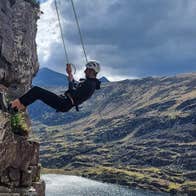 A man abseiling down a rock face with dramatic mountain and sky view in the background